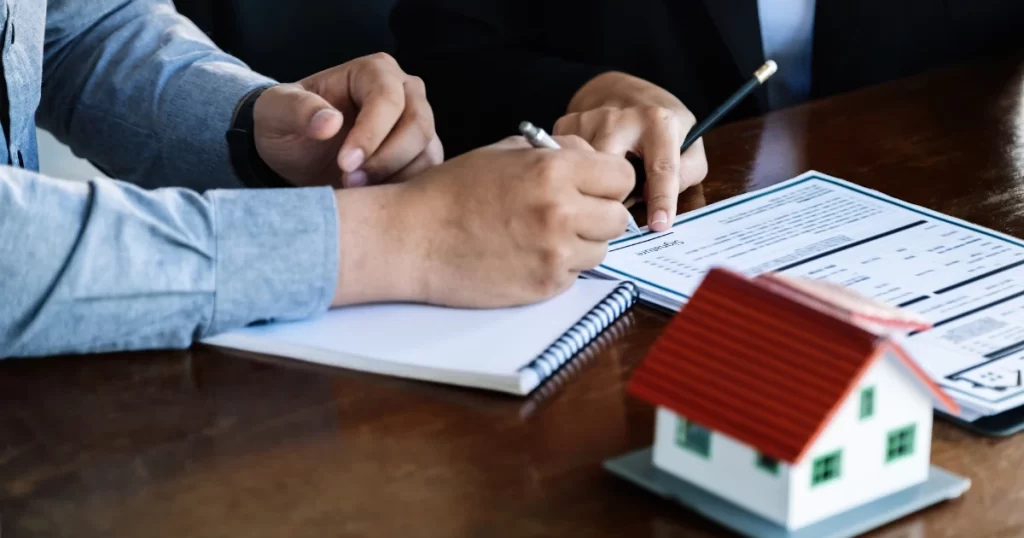 2026土地繼承過戶費用解析主題圖，雙方在文件上簽署資料，桌上擺放房屋模型